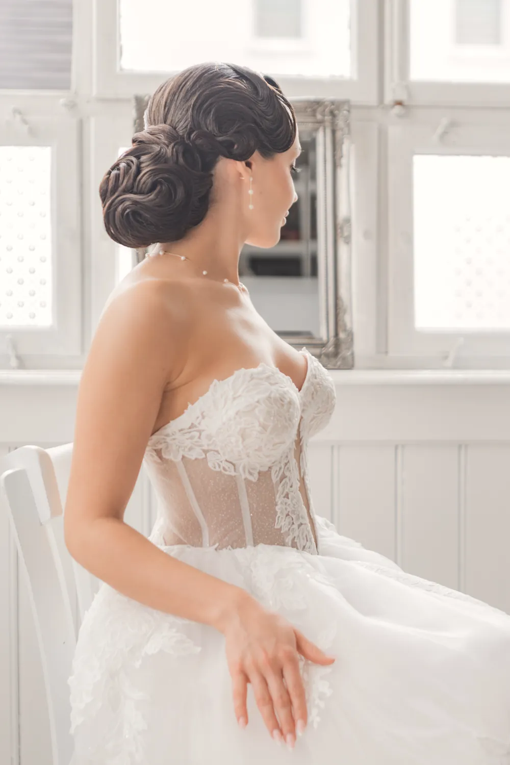 Inspirierendes Brautmotiv: Braut im spitzenbesetzten Kleid am hellen Fenster